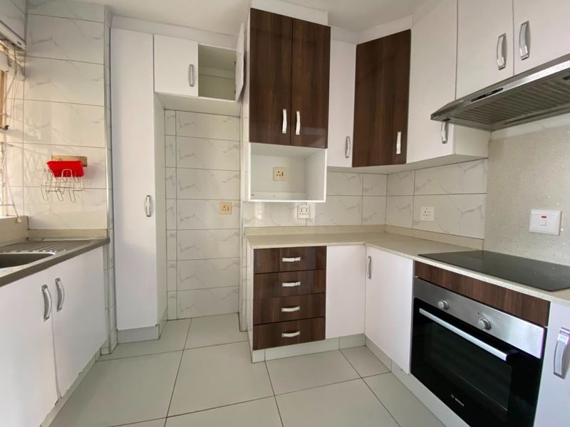 Modern kitchen featuring two-tone cabinetry, stone countertops, built-in oven, electric hob, extractor fan, and tiled finishes throughout.