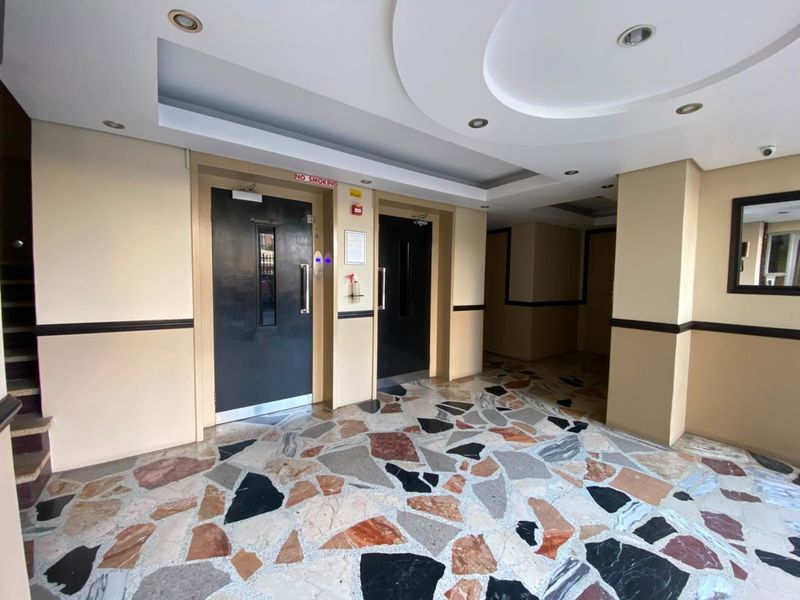 A clean and well-maintained apartment building entrance lobby featuring terrazzo flooring, recessed ceiling lighting, and dual elevator access.