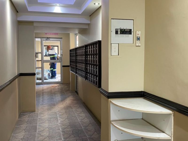 A well-lit apartment building hallway featuring tiled flooring, a bank of mailboxes, and a built-in electrical distribution board.