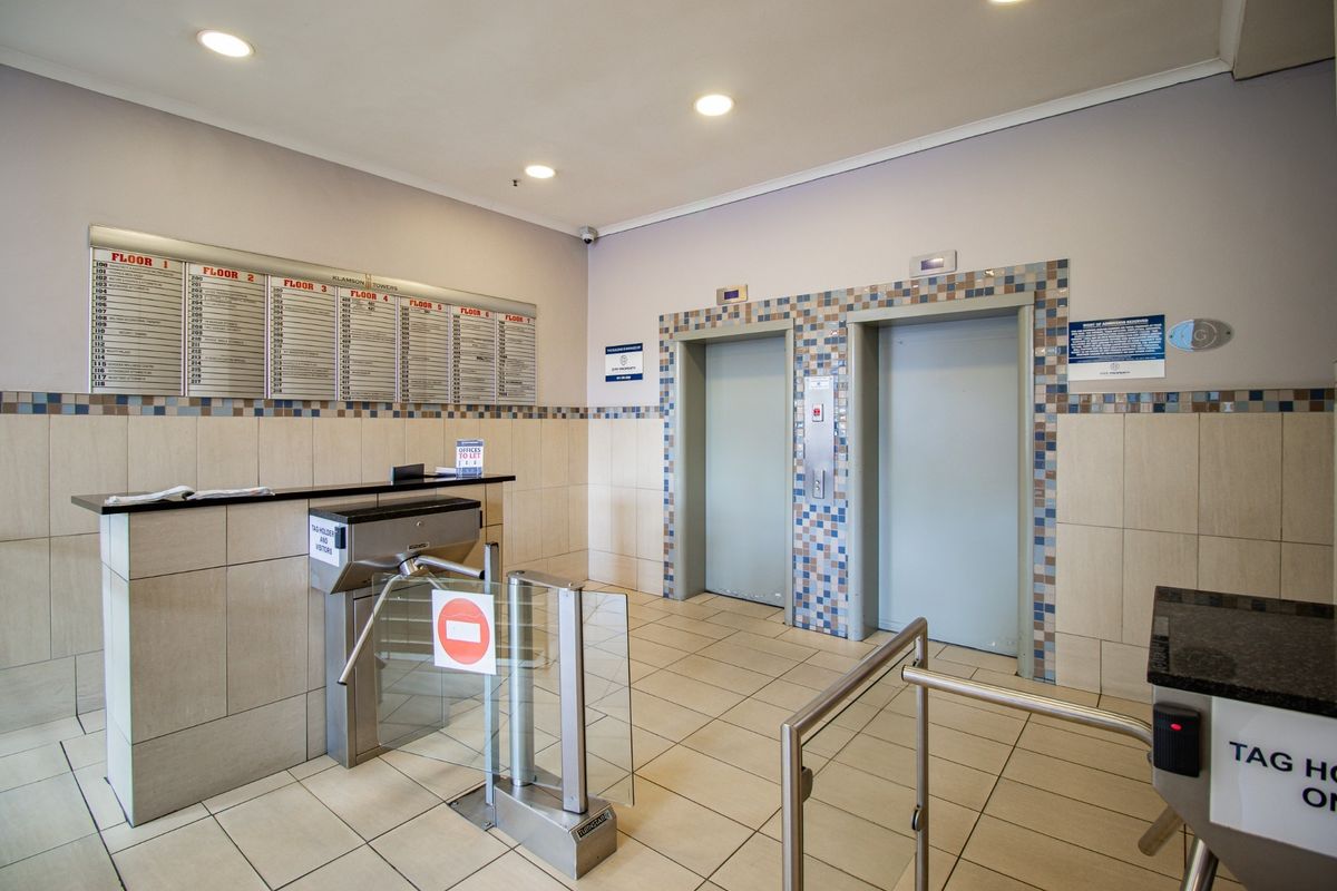 Commercial building lobby featuring a reception desk, security turnstiles, and dual elevator access with a directory board for office tenants.