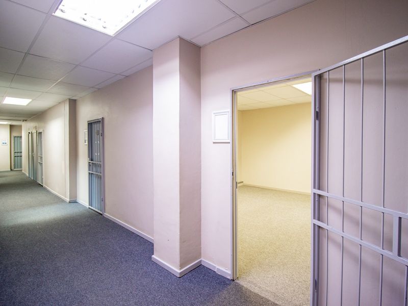A commercial hallway featuring carpeted flooring, suspended ceilings with recessed lighting, and multiple access points secured by metal security gates.