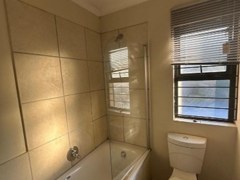 A functional bathroom featuring a bathtub with a glass screen, toilet, and basin, with tiled walls and a window providing natural light.