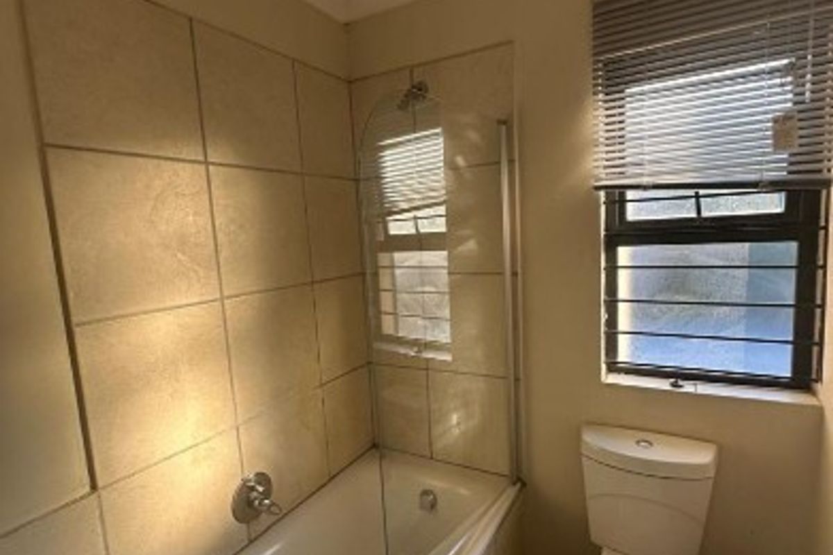 A functional bathroom featuring a bathtub with a glass screen, toilet, and basin, with tiled walls and a window providing natural light.