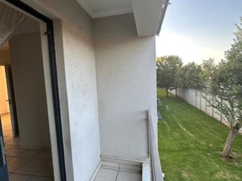 A clean, tiled balcony featuring a metal balustrade, offering an outdoor space with views of the surrounding garden area.