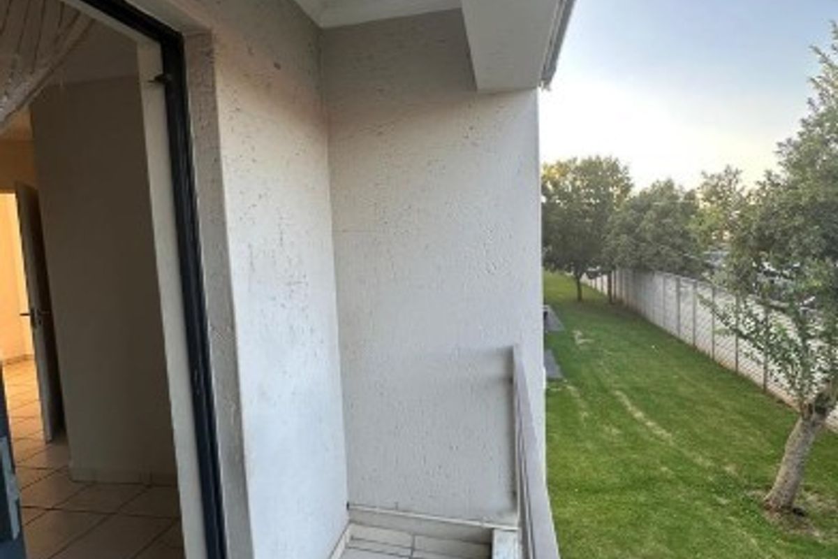 A clean, tiled balcony featuring a metal balustrade, offering an outdoor space with views of the surrounding garden area.