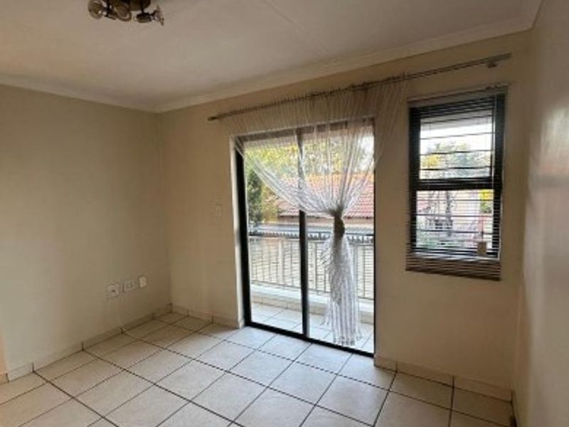 An empty bedroom featuring tiled flooring, a sliding glass door leading to a balcony, and a window with security bars.