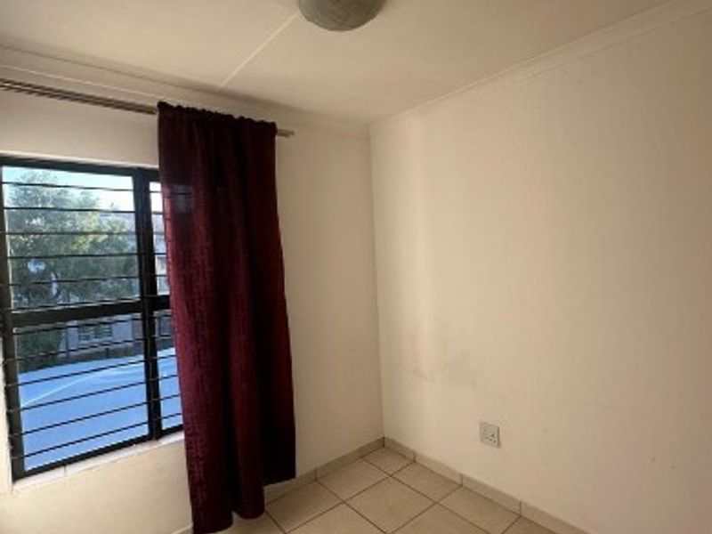 An empty bedroom featuring tiled flooring, a window with security bars, and a ceiling light fixture. The walls show signs of wear.