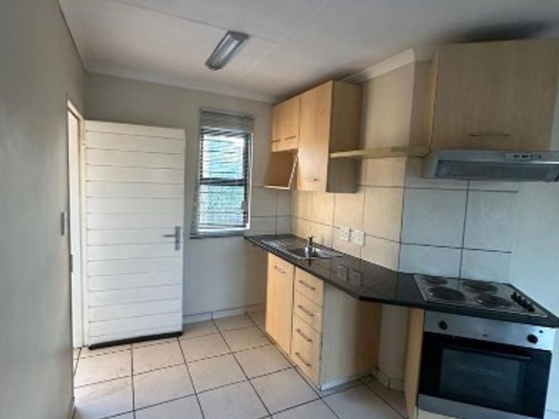 A functional kitchen featuring built-in cabinetry, laminate countertops, a built-in oven with hob, and tiled flooring. The space is currently vacant.