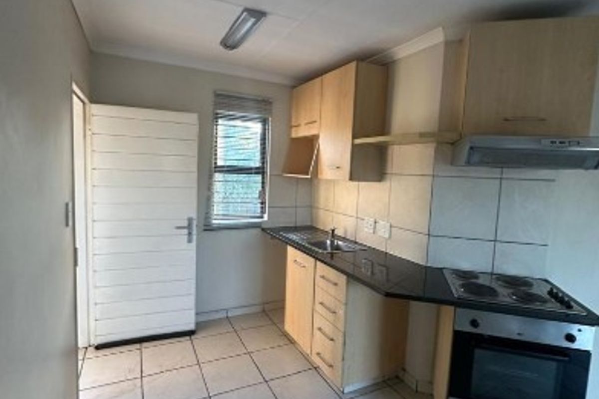 A functional kitchen featuring built-in cabinetry, laminate countertops, a built-in oven with hob, and tiled flooring. The space is currently vacant.