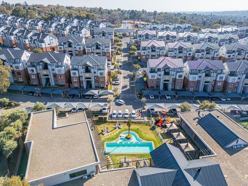 Aerial view of a residential apartment complex featuring a communal swimming pool, landscaped gardens, playground, and covered parking bays.