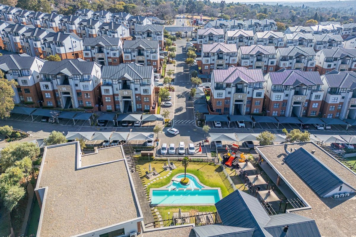 Aerial view of a residential apartment complex featuring a communal swimming pool, landscaped gardens, playground, and covered parking bays.