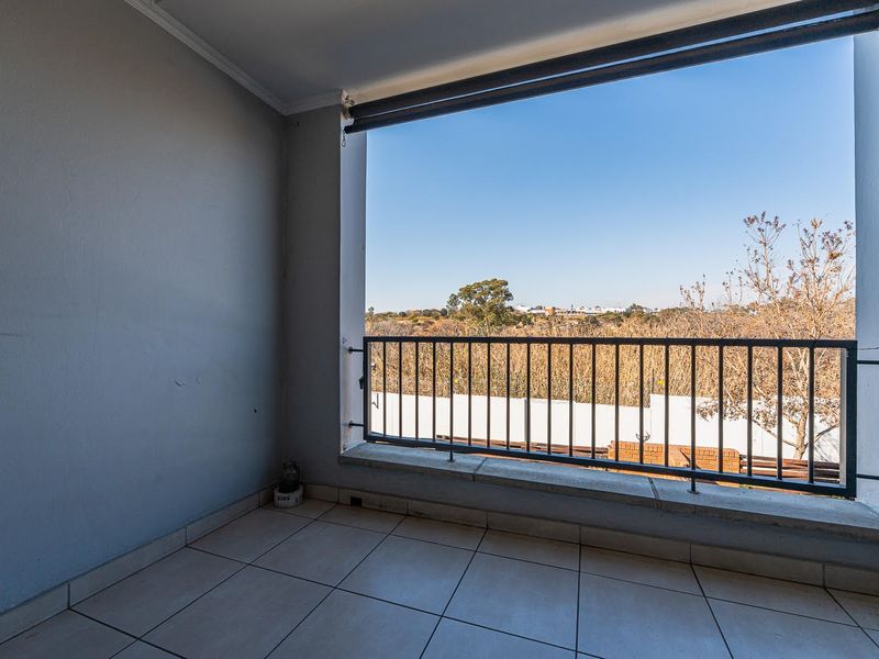 A covered balcony featuring tiled flooring and a metal balustrade, offering an open view of the surrounding landscape.