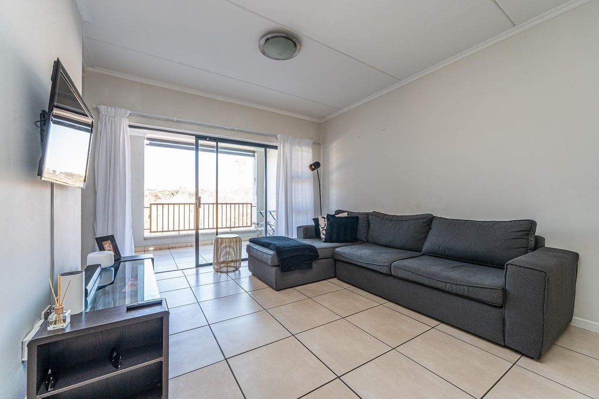A bright living room featuring neutral tiled flooring and a large sliding glass door providing access to an outdoor balcony area.