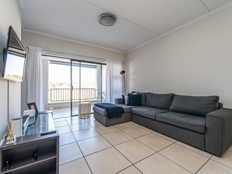 A bright living room featuring neutral tiled flooring and a large sliding glass door providing access to an outdoor balcony area.