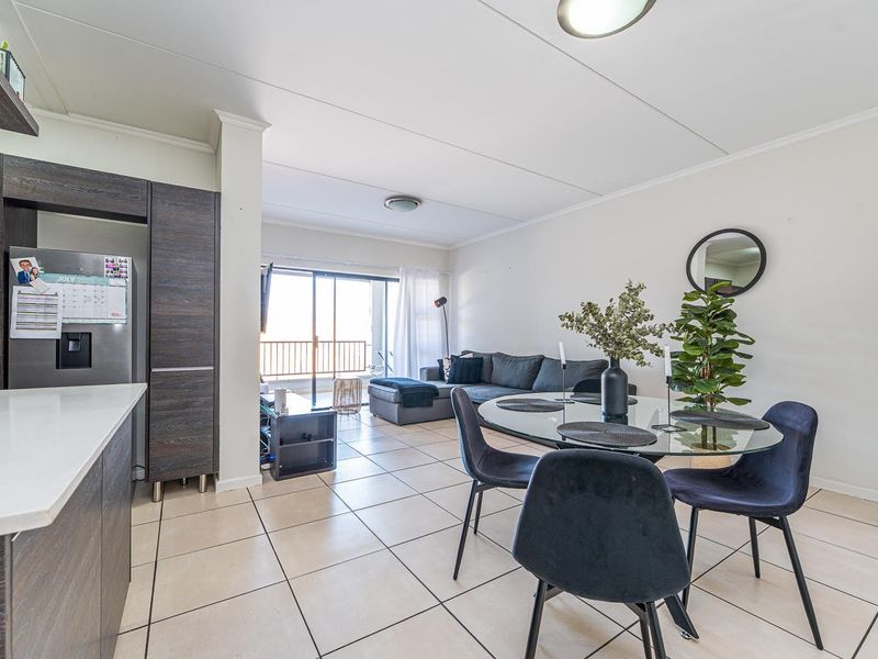 Open-plan living and dining area featuring tiled flooring, modern kitchen cabinetry with stone countertops, and direct access to a balcony through sliding glass doors.