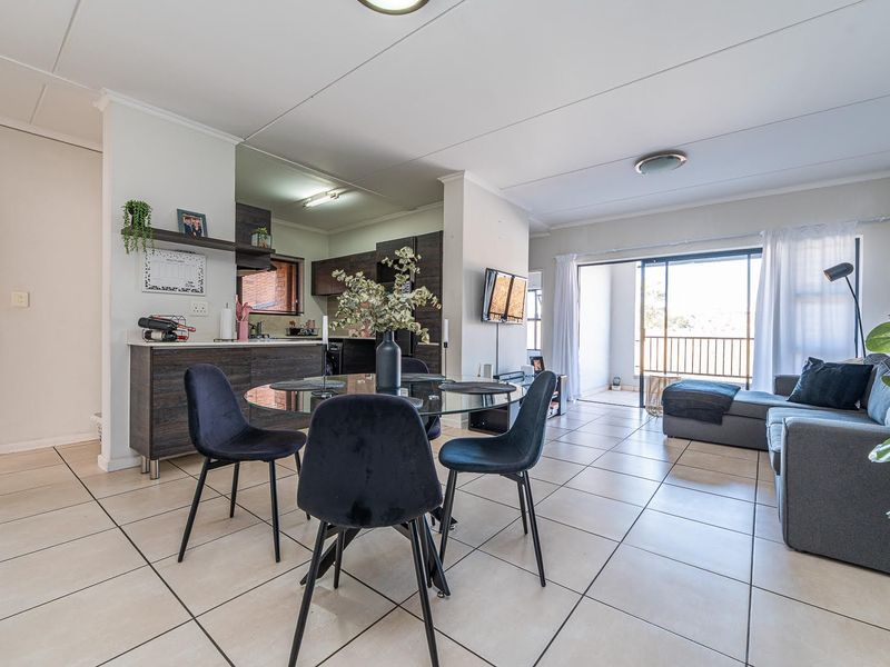 Open-plan living and dining area featuring tiled flooring, a modern kitchen with dark cabinetry, and a sliding door leading to a balcony.