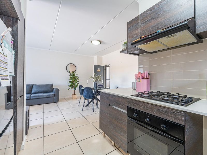 Open-plan living area featuring a modern kitchen with dark wood cabinetry, gas hob, built-in oven, and tiled flooring throughout the combined space.
