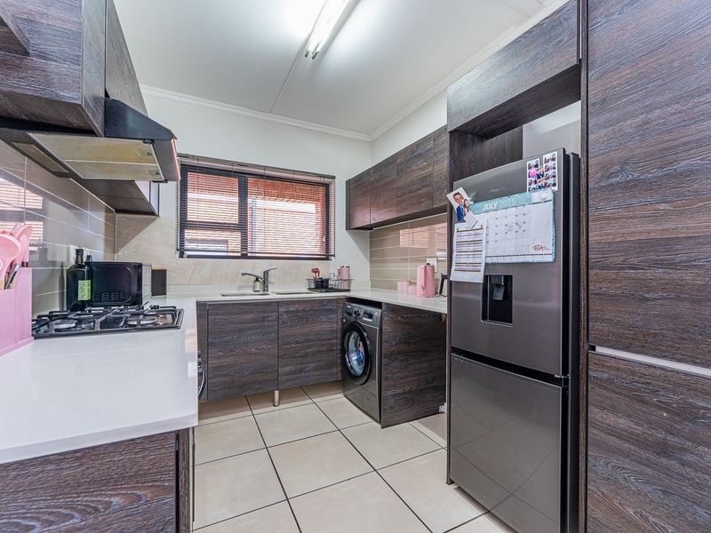 Modern kitchen featuring dark wood-grain cabinetry, stone-look countertops, a gas hob with extractor, and integrated laundry plumbing.