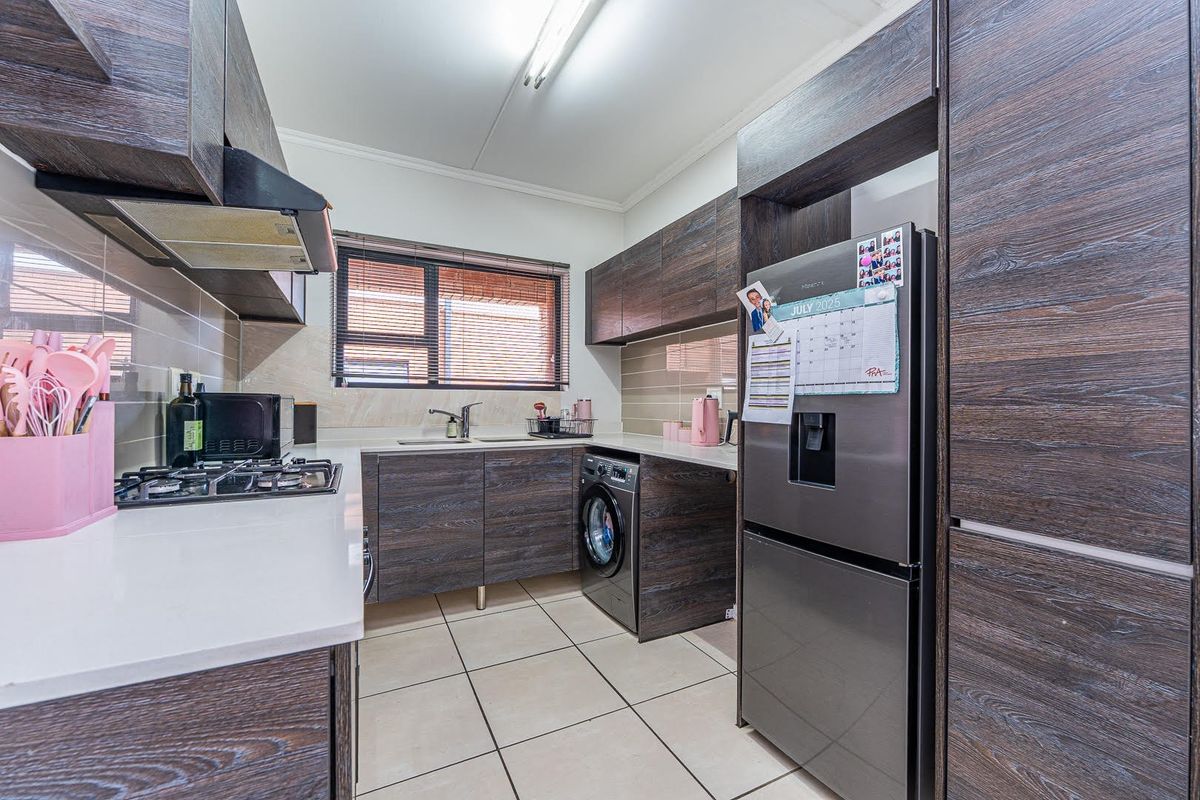 Modern kitchen featuring dark wood-grain cabinetry, stone-look countertops, a gas hob with extractor, and integrated laundry plumbing.