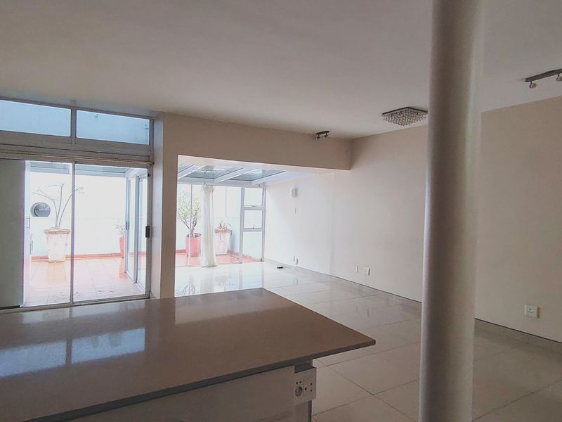 Spacious open-plan living area featuring tiled floors, a central structural column, and large sliding glass doors leading to an outdoor patio space.