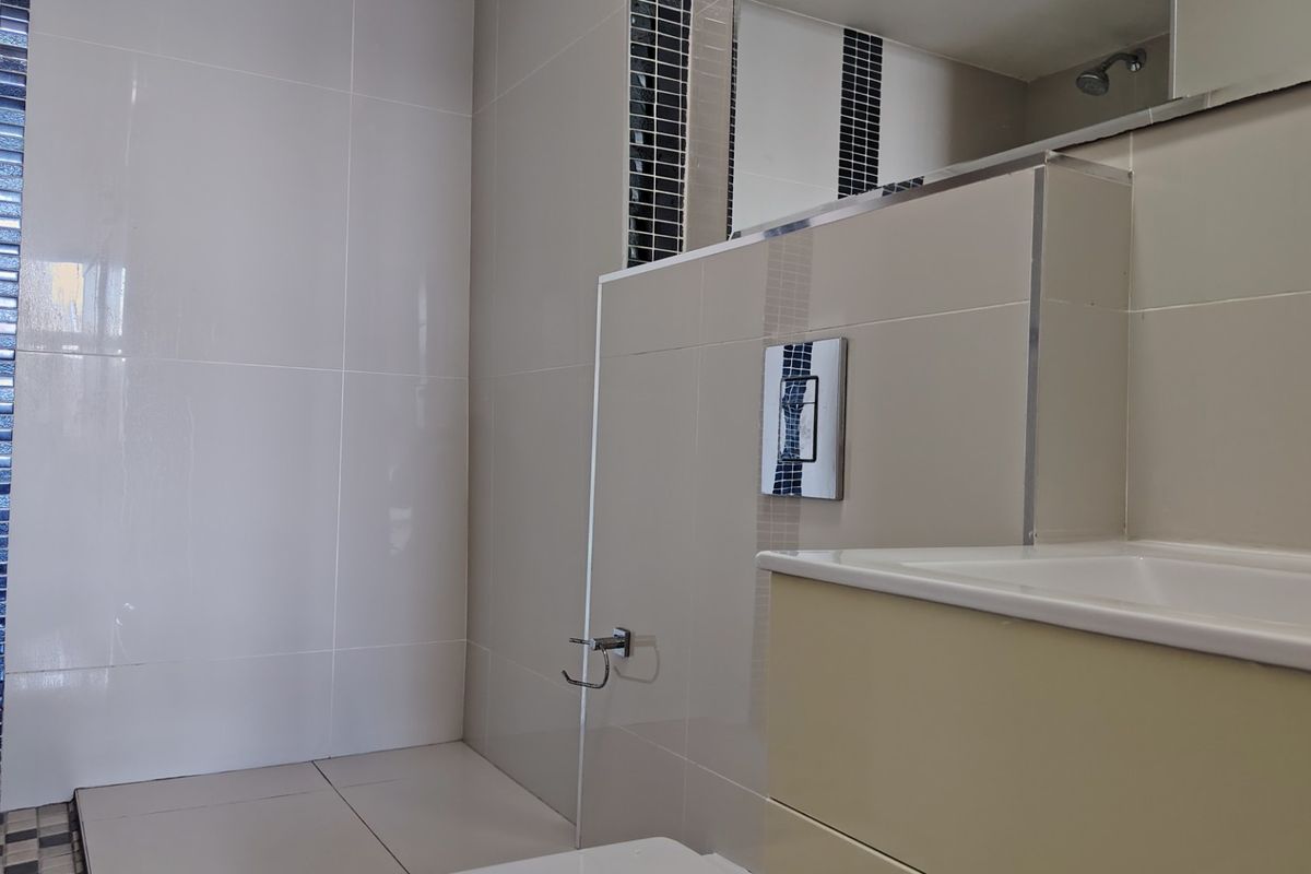 A modern bathroom featuring neutral wall tiles with a decorative mosaic accent strip, a vanity basin with chrome tapware, and a wall-mounted flush system.