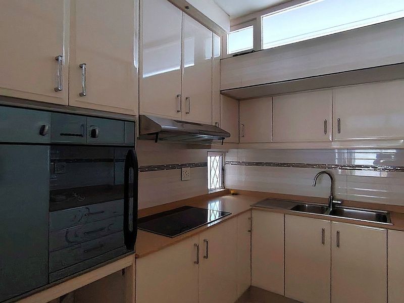 A clean, functional kitchen featuring high-gloss cabinetry, integrated oven, electric cooktop, and a stainless steel sink with a tiled backsplash.