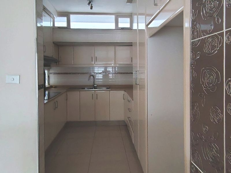 A functional kitchen featuring neutral built-in cabinetry, tiled flooring, and a tiled backsplash, offering a clean and practical workspace.