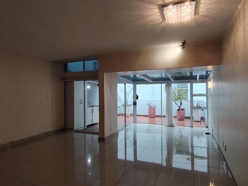 Spacious open-plan living area featuring polished tile flooring, modern recessed lighting, and seamless access to a glass-roofed patio area.