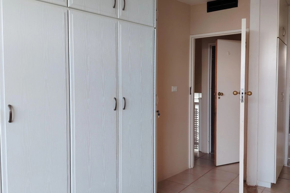A bedroom interior featuring built-in white cupboards and tiled flooring, leading to an adjacent hallway area.