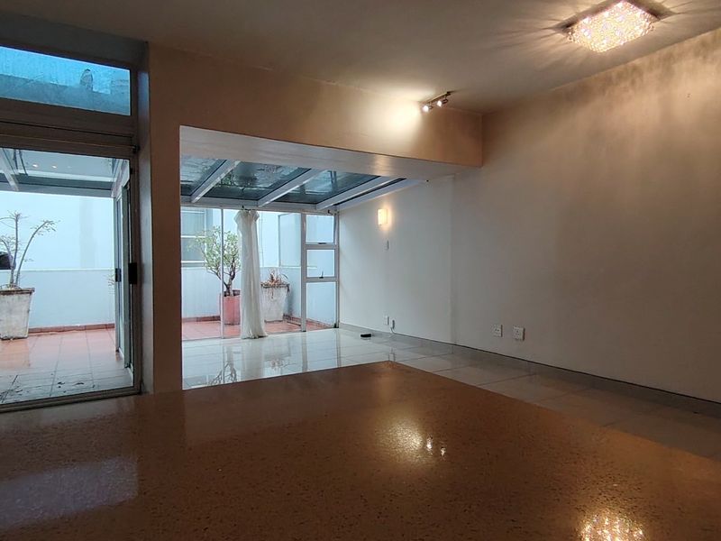 Spacious open-plan living area featuring polished tiled floors, a unique glass roof section, and large sliding doors leading to an outdoor patio.