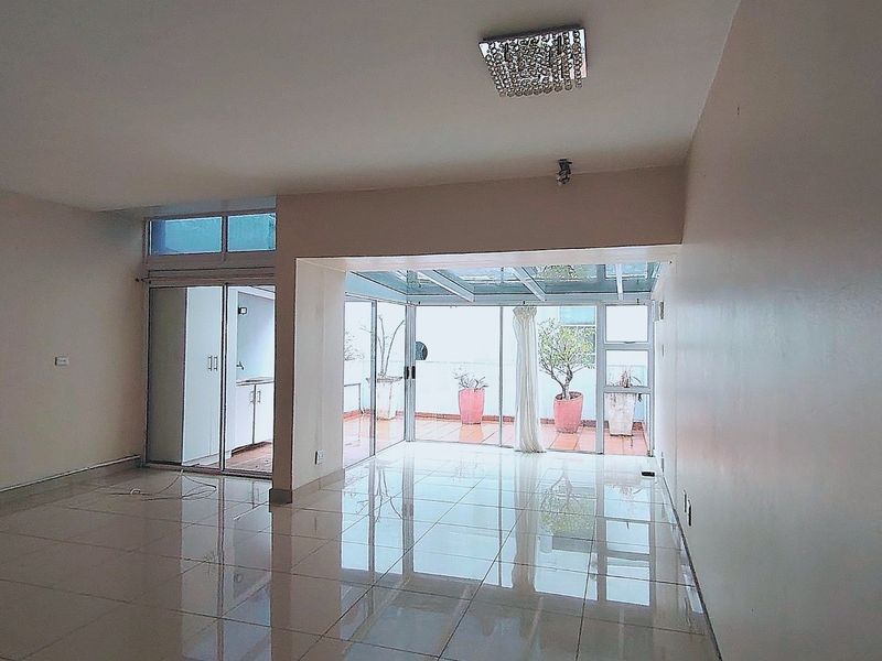 Spacious, empty living area featuring polished tile floors, modern glass sliding doors, and a bright glass-roofed patio extension.