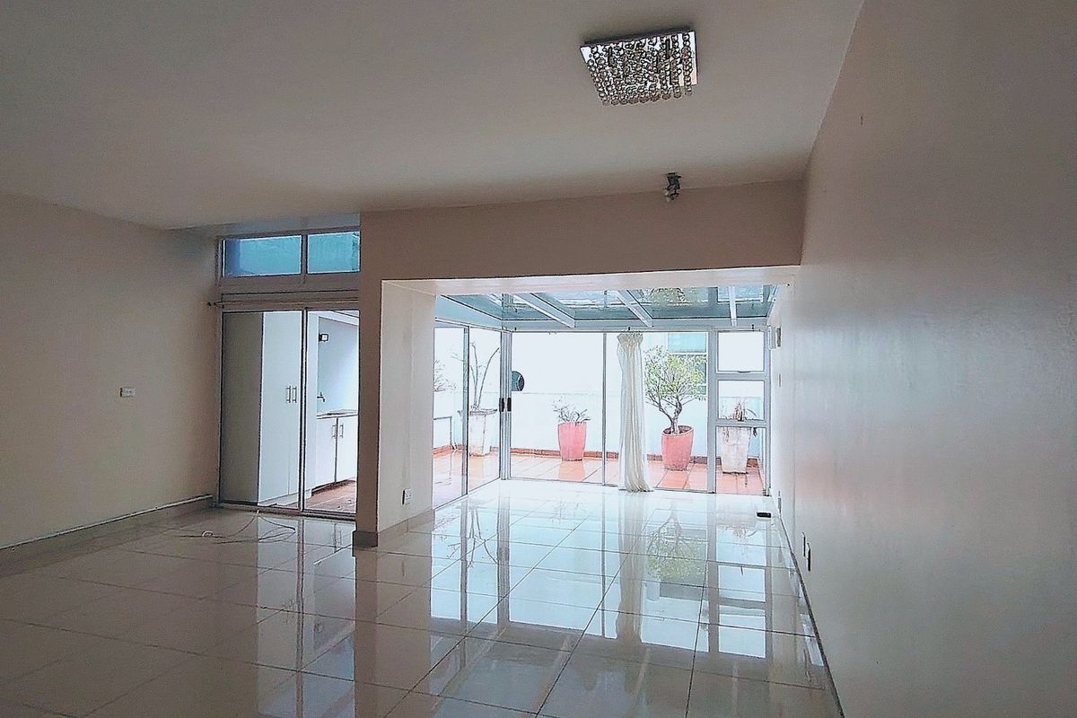 Spacious, empty living area featuring polished tile floors, modern glass sliding doors, and a bright glass-roofed patio extension.