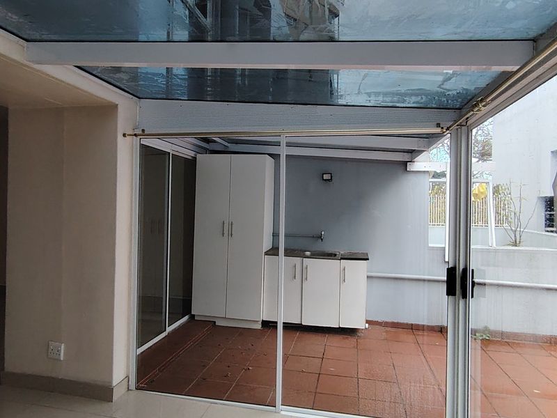 A covered patio area featuring a glass roof, sliding glass doors, built-in cabinetry with a sink, and tiled flooring.