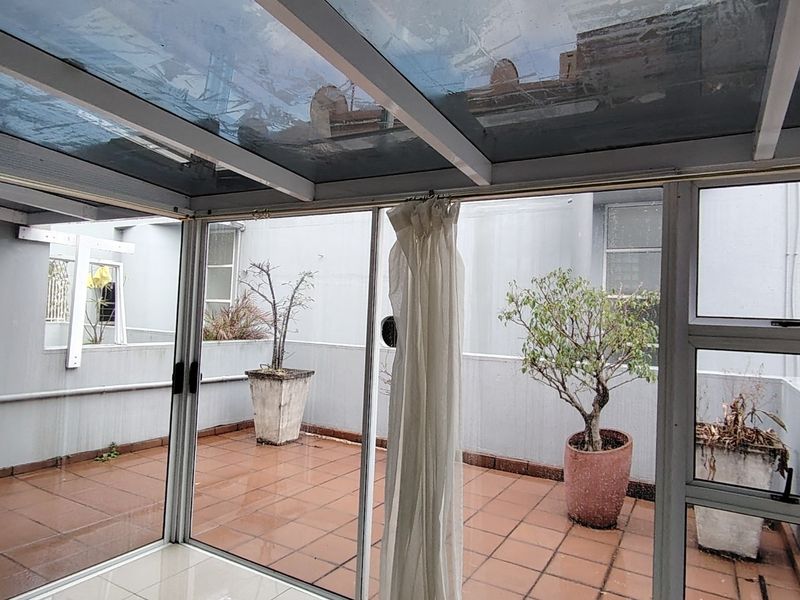 Enclosed patio area featuring a glass roof, tiled flooring, and sliding glass doors leading to an open-air terrace space.