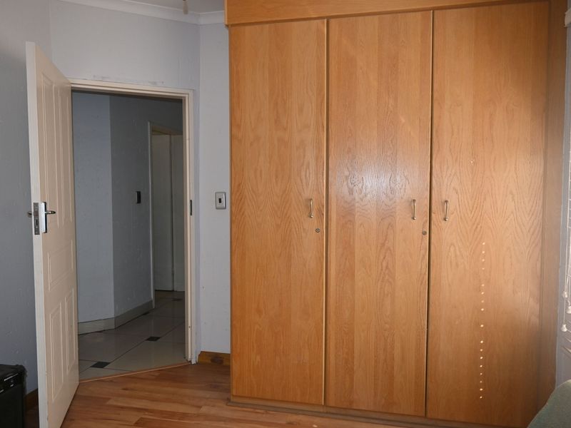 A bedroom featuring light wood-finish built-in wardrobes, laminate flooring, and venetian blinds, offering a functional space ready for personalization.
