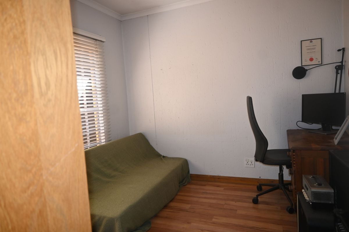 A functional bedroom or home office space featuring laminate flooring, venetian blinds, and standard electrical fixtures.