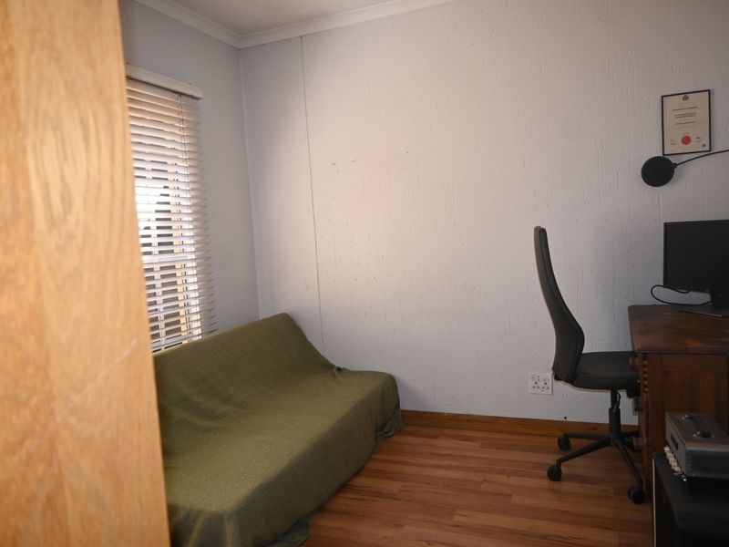 A functional bedroom or home office space featuring laminate flooring, venetian blinds, and standard electrical fixtures.