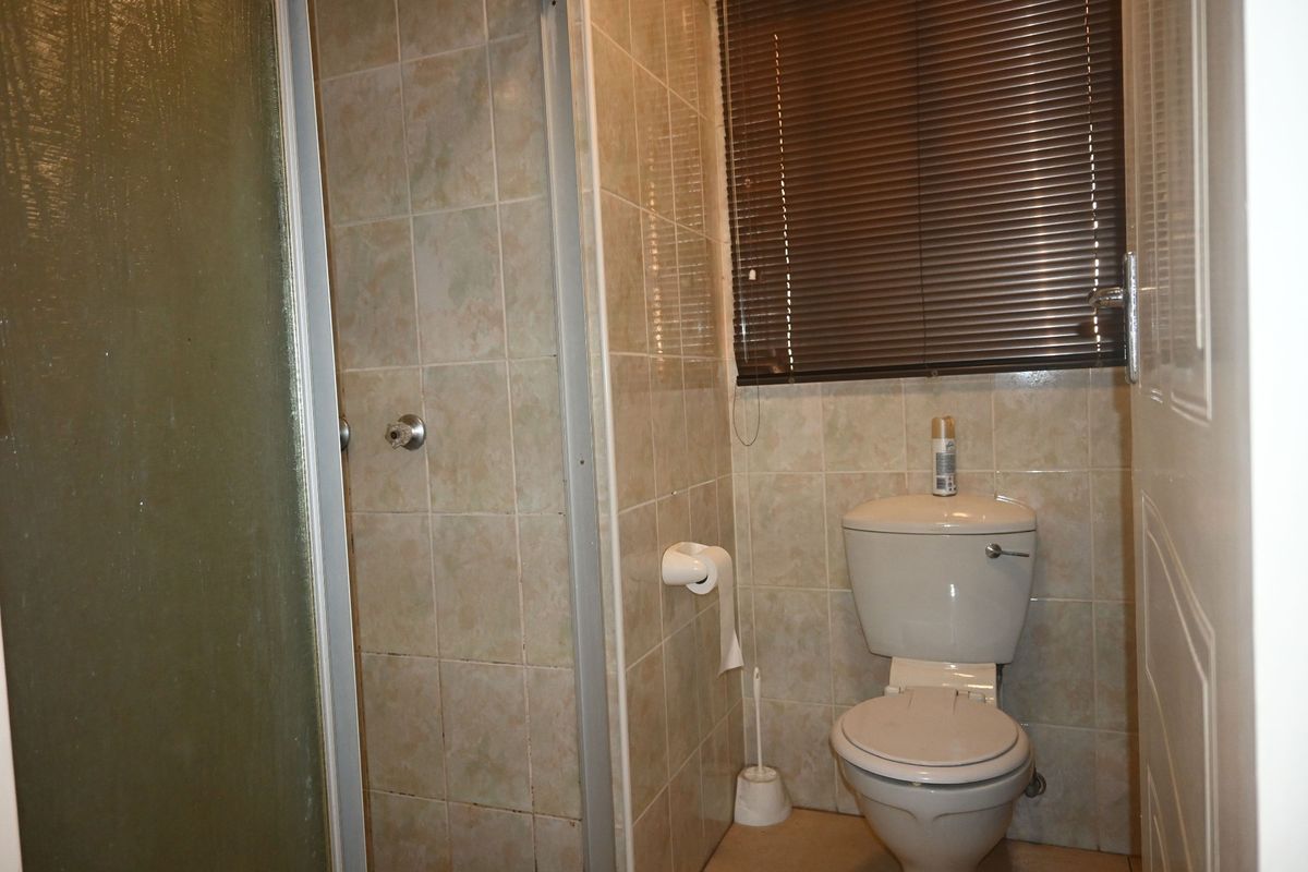 A compact bathroom featuring a shower enclosure, toilet, and tiled wall finishes with venetian blinds.
