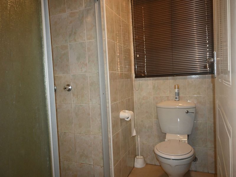 A compact bathroom featuring a shower enclosure, toilet, and tiled wall finishes with venetian blinds.