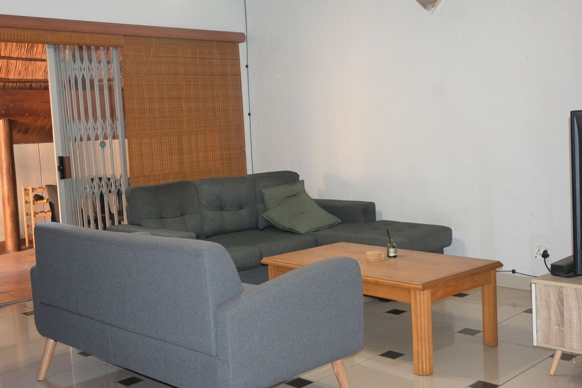 A living room area featuring tiled flooring and a sliding security gate leading to an outdoor patio space.