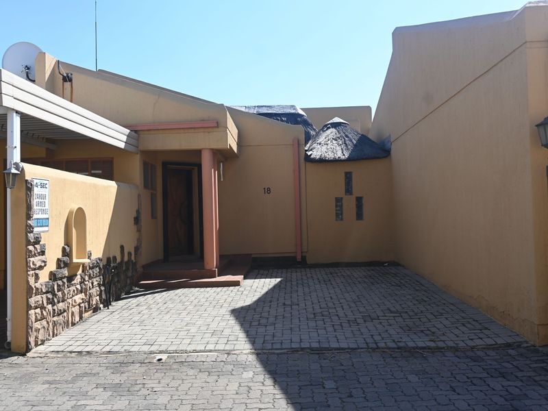 Front entrance of the townhouse featuring a paved driveway, carport, and distinctive thatched roof detailing with stone-clad accents.