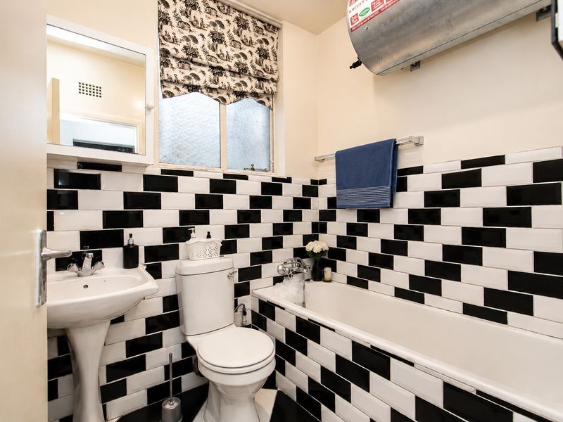 A bathroom featuring a black and white tiled wall design, pedestal basin, toilet, and a bathtub with a wall-mounted geyser.