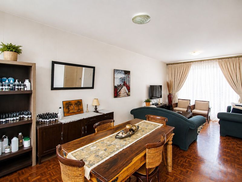 An open-plan living and dining area featuring classic parquet flooring and large windows with curtain treatments, offering a functional and well-lit living space.