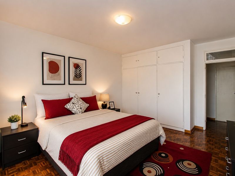 A well-maintained bedroom featuring classic parquet flooring, ample built-in cupboard storage, and a bright, neutral interior layout.