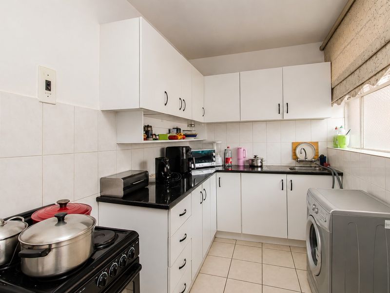 A functional kitchen featuring white cabinetry, black granite countertops, tiled backsplash, and tiled flooring, with space for a washing machine.