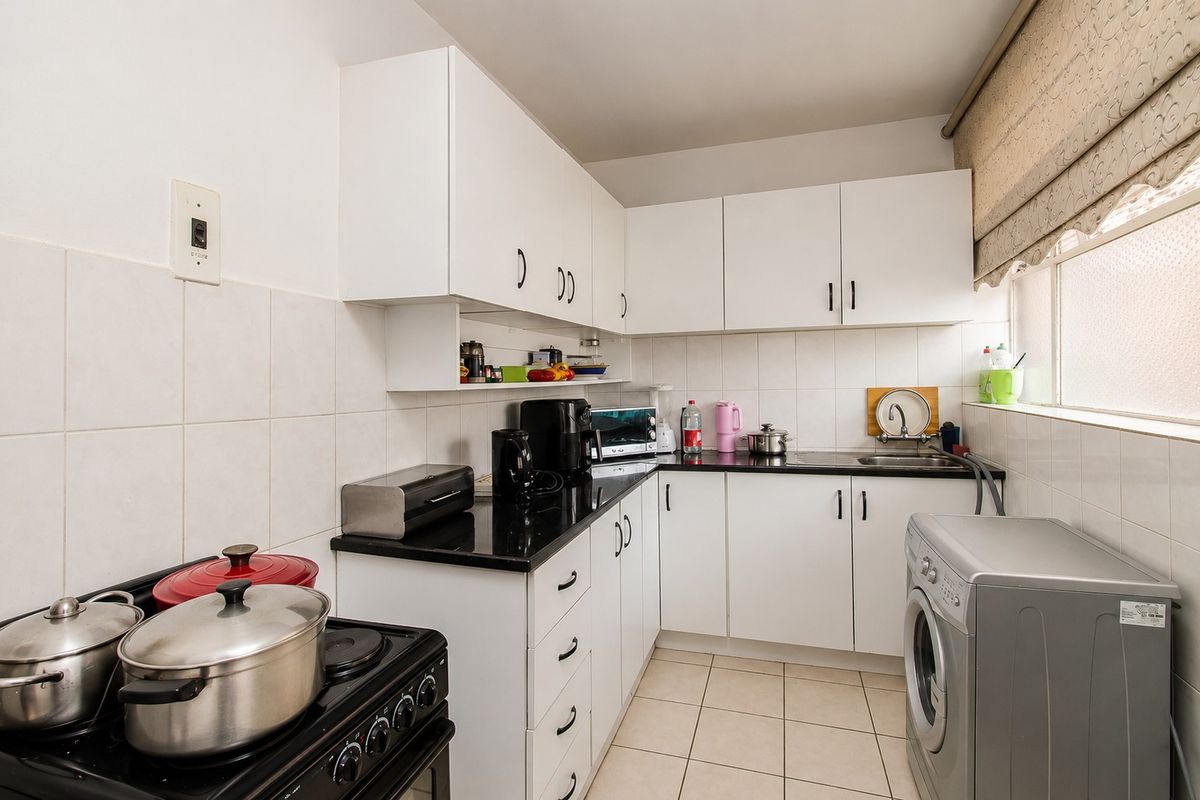 A functional kitchen featuring white cabinetry, black granite countertops, tiled backsplash, and tiled flooring, with space for a washing machine.