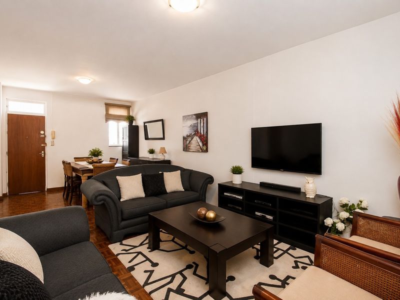Open-plan living and dining area featuring warm parquet flooring and neutral walls, providing a functional and well-lit space for daily living.