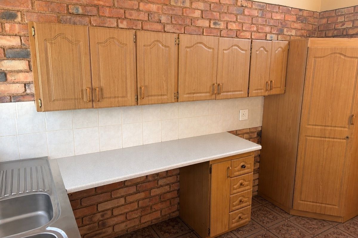 A functional kitchen area featuring wood-look cabinetry, a stainless steel double sink, and a distinctive exposed brick wall finish.