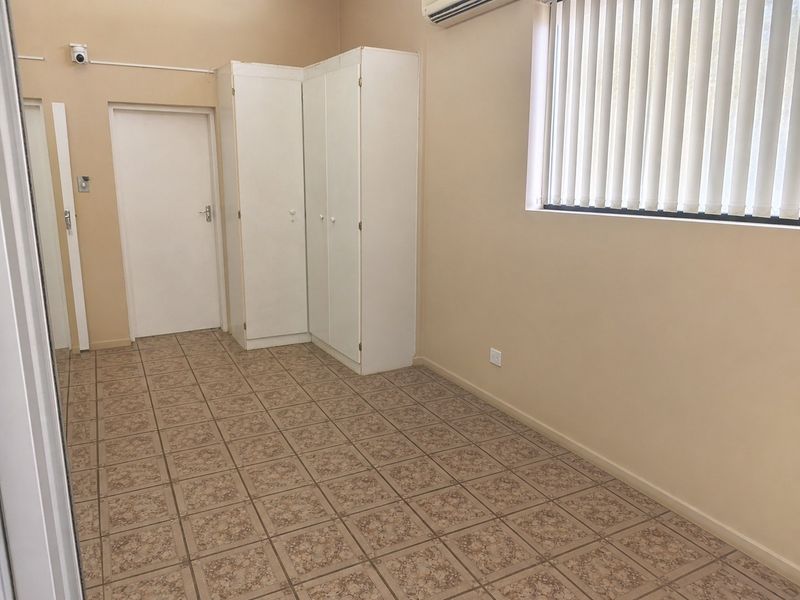 A clean, empty bedroom featuring tiled flooring, built-in cupboards, an air conditioning unit, and vertical blinds.