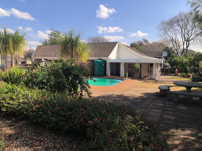Rear exterior view featuring a swimming pool, paved patio area, and a water tank set within a landscaped garden.